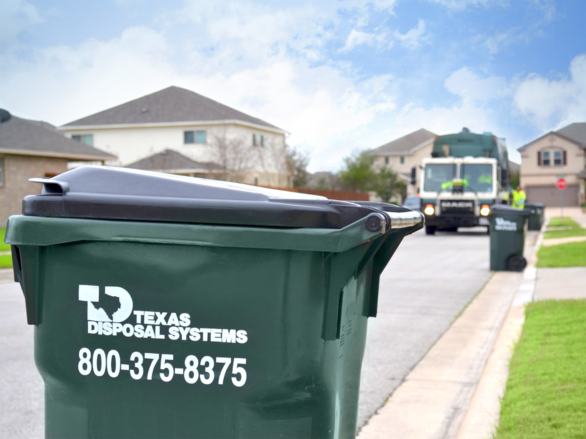 Waste cart with Texas Disposal Systems logo sitting on the curb.