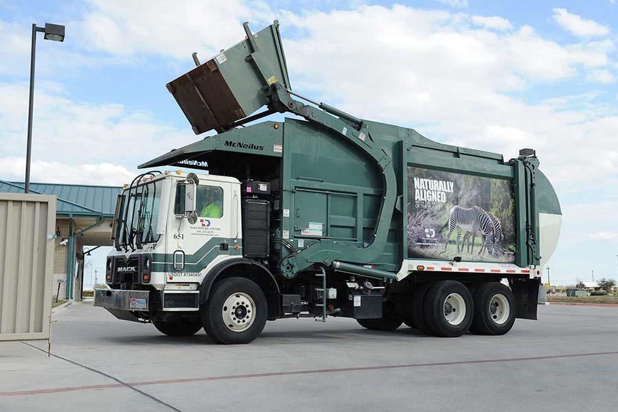 Green front load dumpster truck picking up front load dumpster at a building