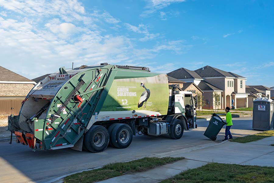 Green TDS pick up truck on neighborhood road with TDS employee with cart in front of TDS grey portable restroom