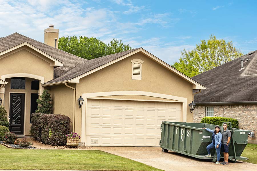 Green TDS mini roll off dumpster in front of house with couple standing in front